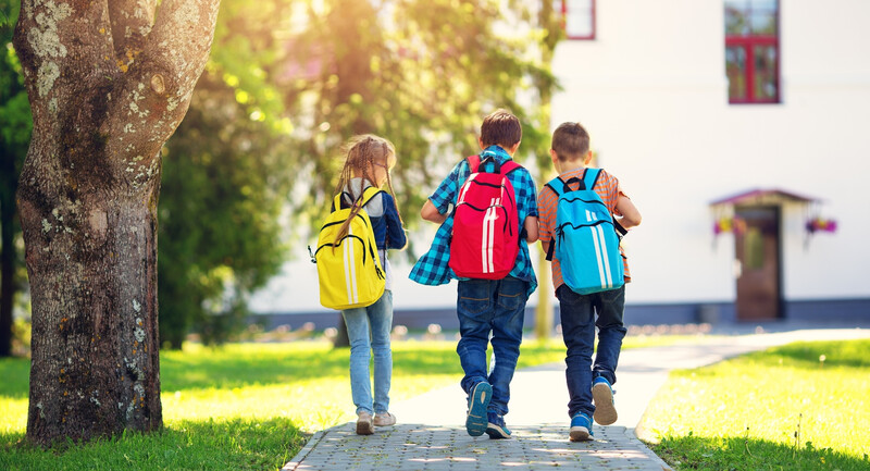 Three children with backpacks happily walking to school.